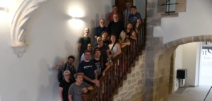 Fotografia dels membres de Softcatalà que van poder acudir a la trobada de pencaires d'estiu 2025 a Sant Mateu, a dalt d'una escalinata de pedra, en l'interior d'un edifici de parets blanques.