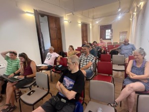 Fotografia d'uns quants membres de Softcatalà reunits a una sala blanca rectangular, amb cadires de colors grisos i vermells i portes de fusta fosca.